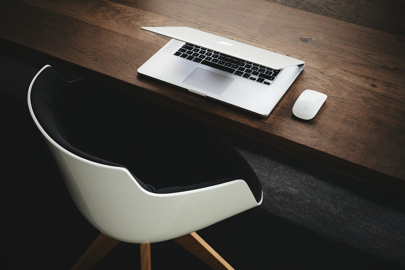 Laptop and mouse on a wooden desk beside a white chair